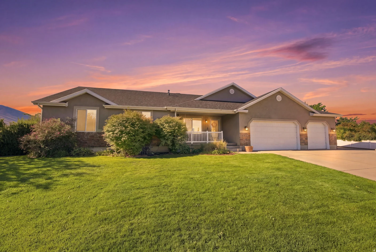 Stucco exterior with stone accents, a covered front porch with white railing, and a multi-car garage with white doors